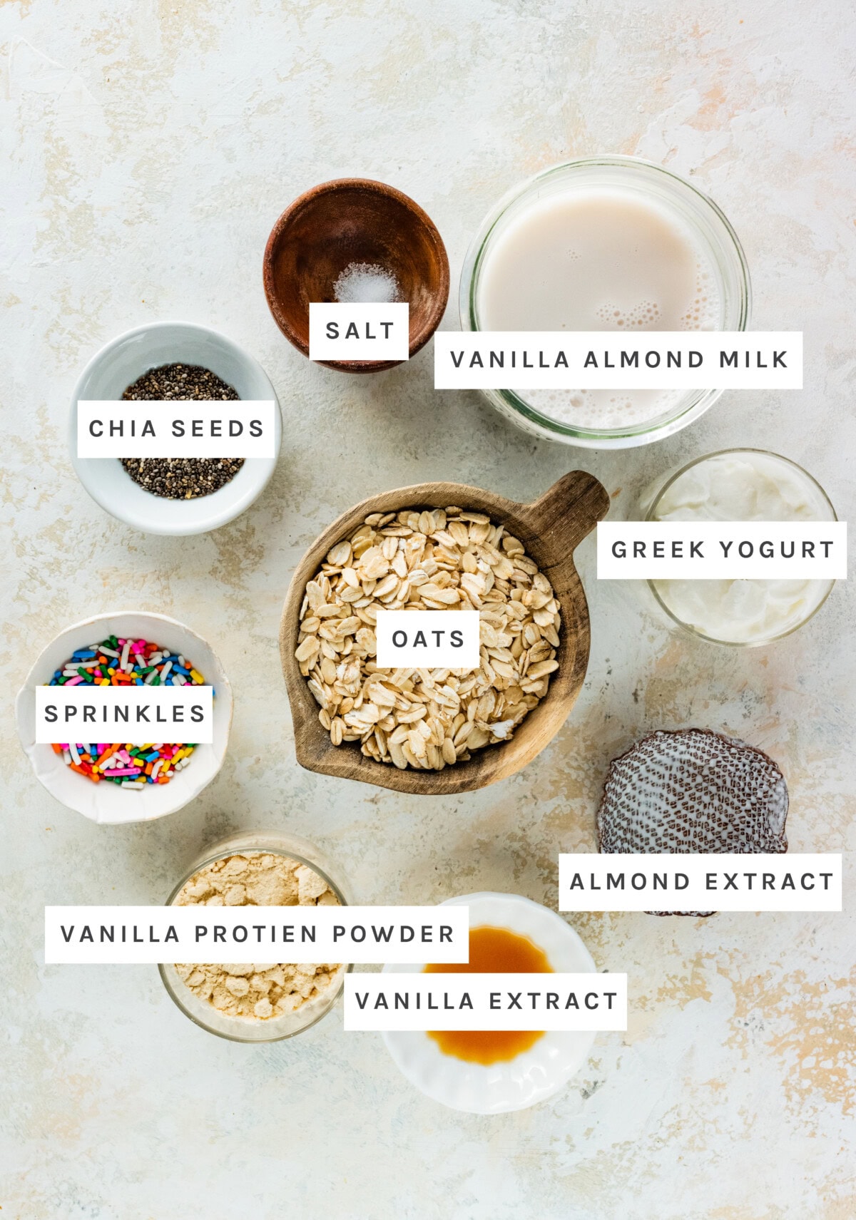 Ingredients measured out to make: Chia Seeds, Vanilla Protein Powder, Vanilla Extract, Almond Extract, Greek Yogurt, Salt, Oats, Sprinkles, Vanilla Almond Milk,