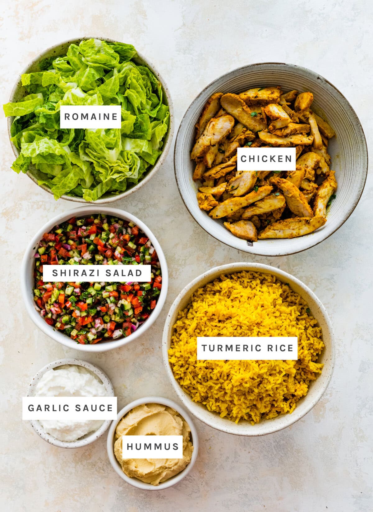 Ingredients measured out to make Chicken Shawarma Bowls: Romaine, Shirazi Salad, Hummus, Garlic Sauce, Chicken, Turmeric Rice