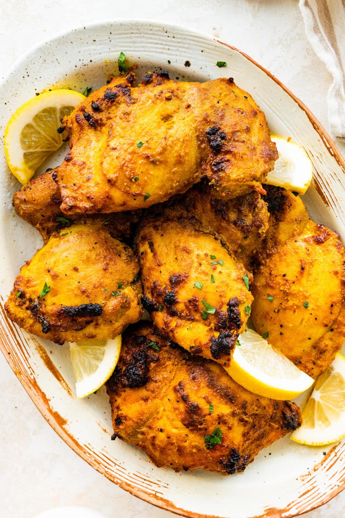 Cooked chicken shawarma served on a platter. The chicken is topped with fresh parsley and served next to lemon slices.