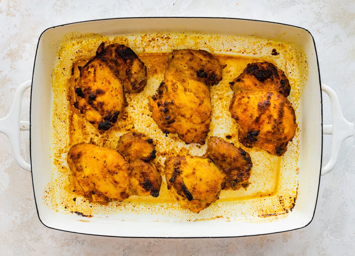 Baked chicken shawarma thighs in the white baking dish.