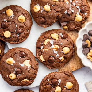 9 chocolate peanut butter cookies spread out on a counter. All of the cookies are topped with flaky sea salt.
