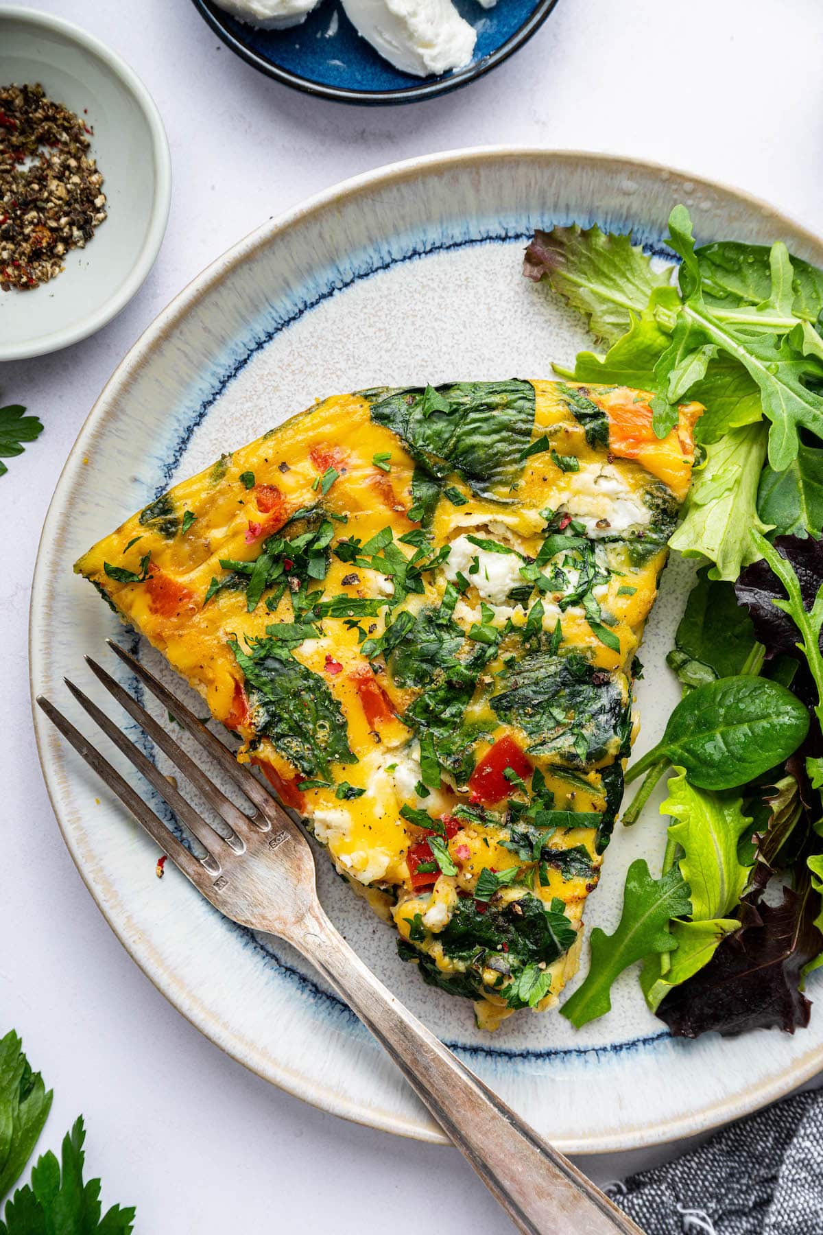 A frittata slice served on a plate with a side salad. There is a silver fork on the plate.
