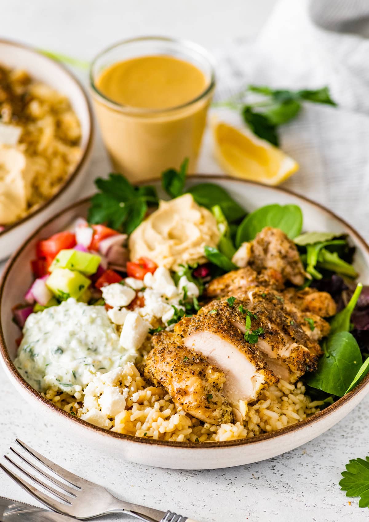 A bowl of Greek chicken, tzatziki, hummus, fresh greens, cucumber tomato salad, and feta cheese.