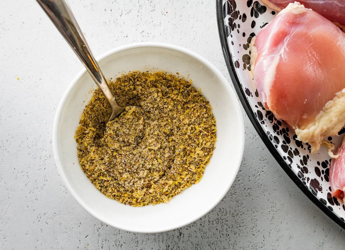 The seasoning mixture for the Greek chicken in a small white bowl with a silver spoon.