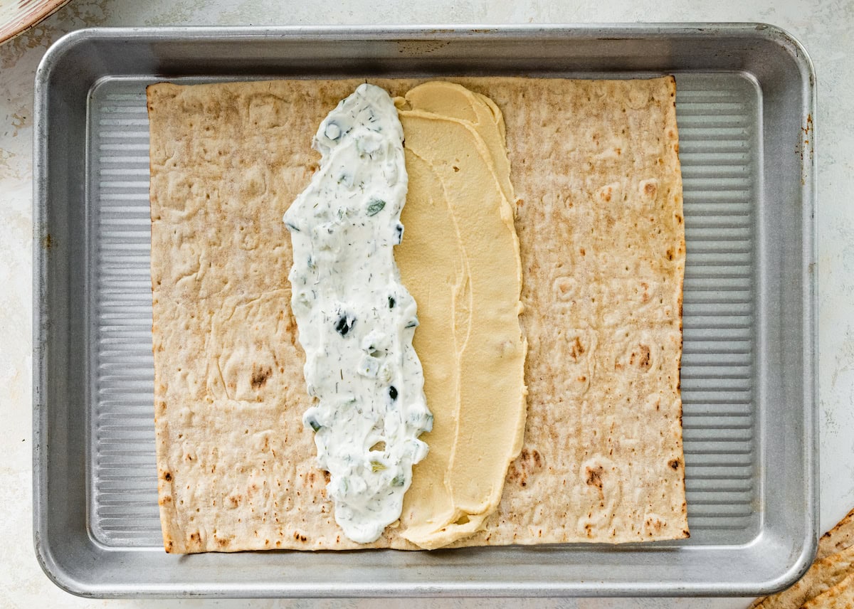 A piece of lavash bread that's been spread with hummus and tzatziki in the middle.