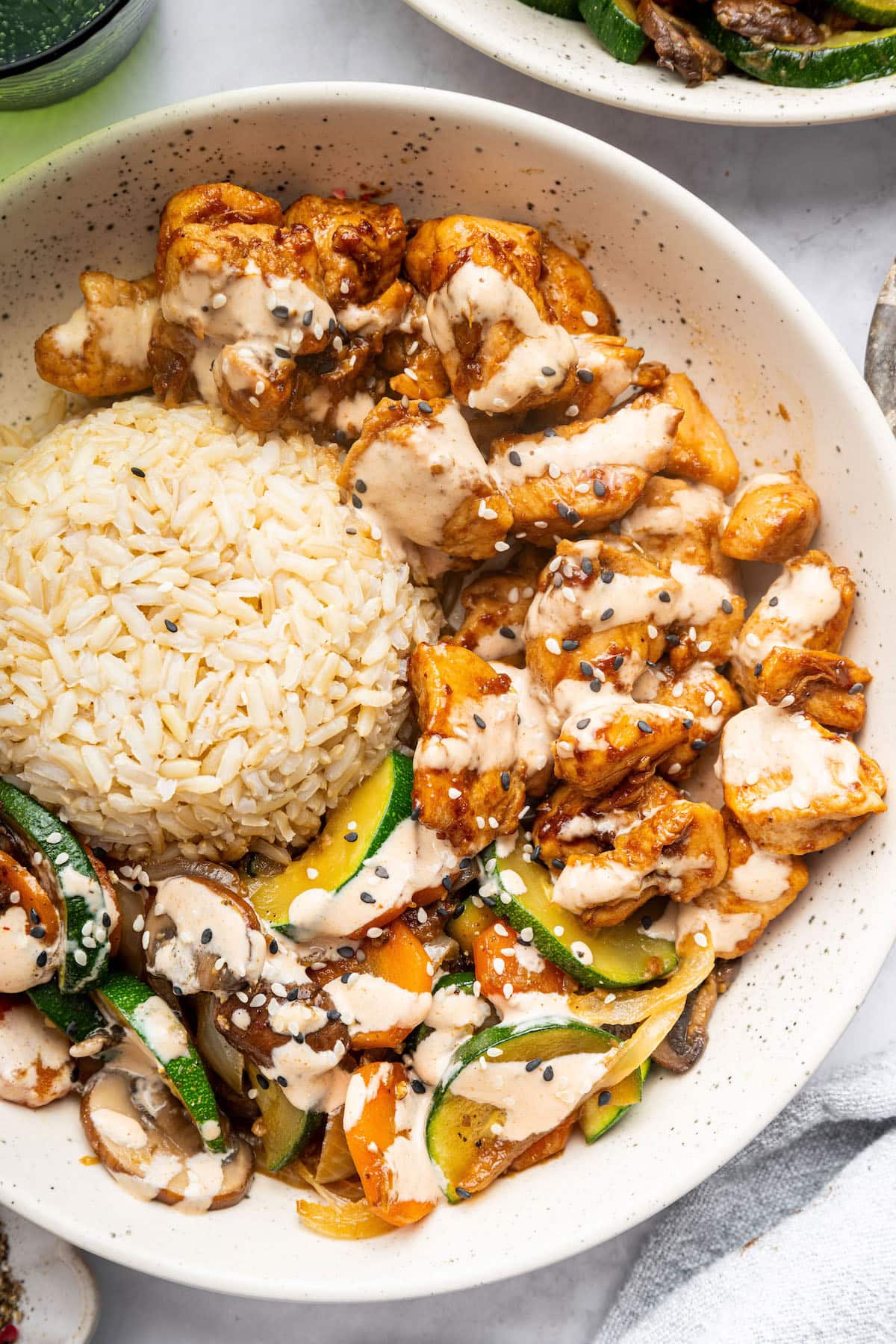 A plate of hibachi-style chicken with a drizzle of creamy sauce, served alongside a mound of brown rice and sautéed vegetables.