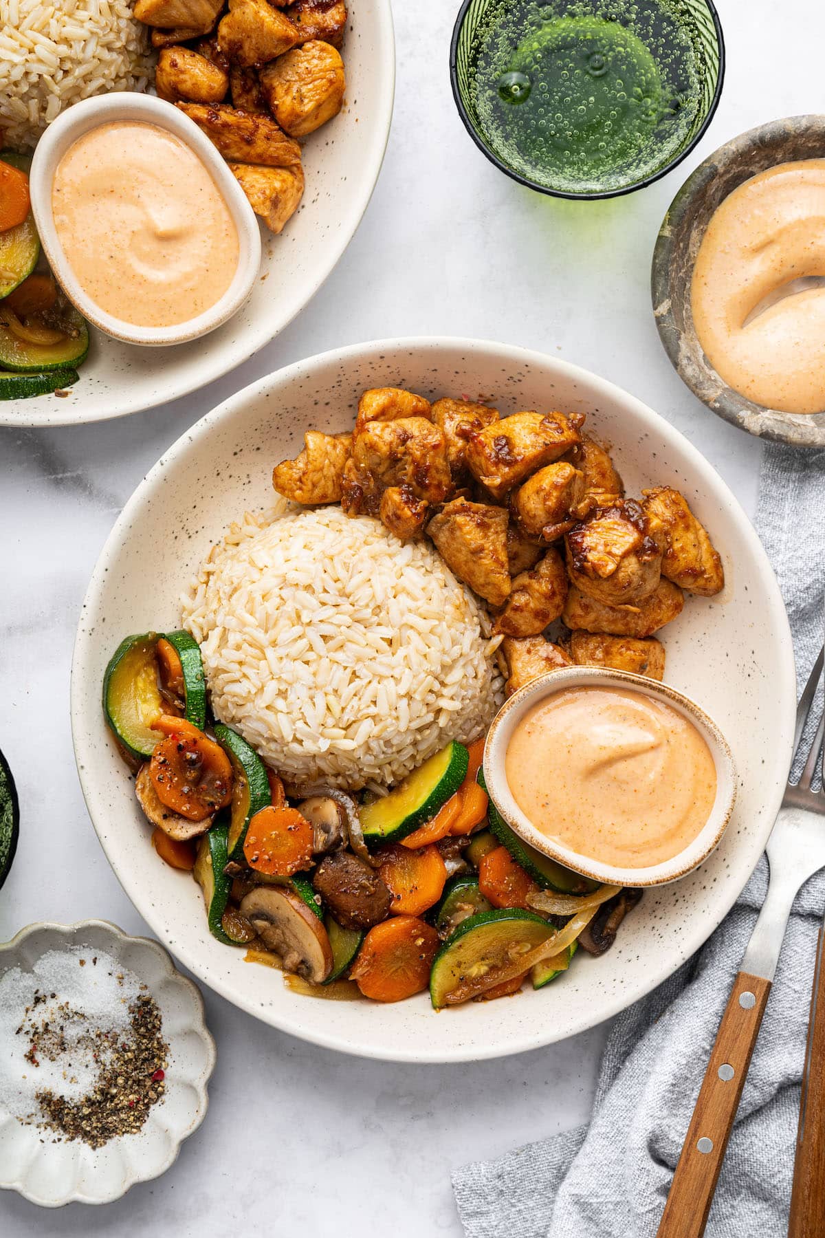 A plate featuring hibachi chicken, brown rice, and sautéed vegetables with a side of creamy dipping sauce.