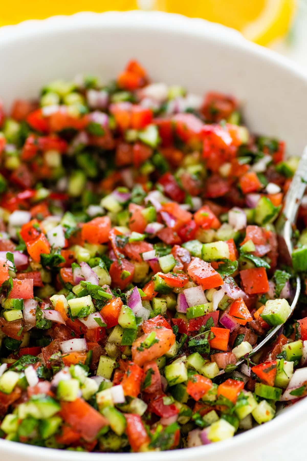 A Shirazi Salad in a white bowl served with a silver spoon.