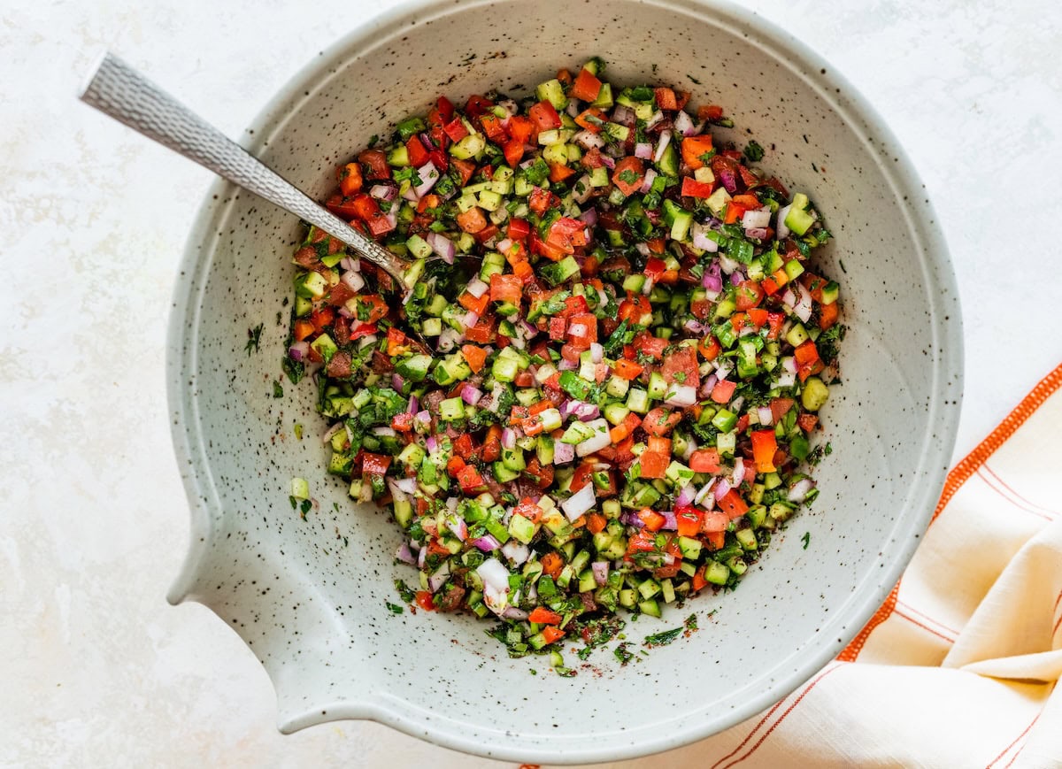 A Shirazi Salad in a mixing bowl served with a silver spoon.
