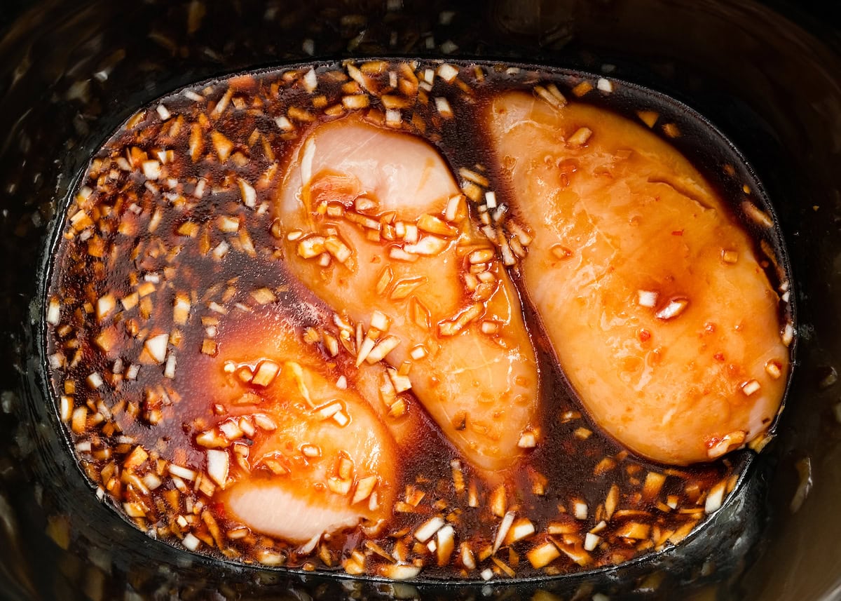 Three chicken breasts in a slow cooker. The chicken is coated with the teriyaki sauce.
