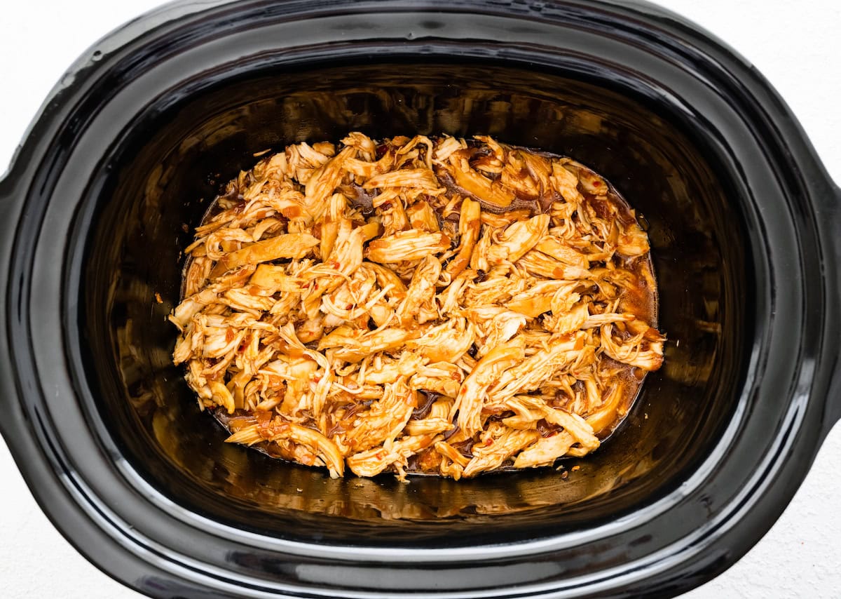 The shredded chicken coated in the teriyaki sauce in the slow cooker.