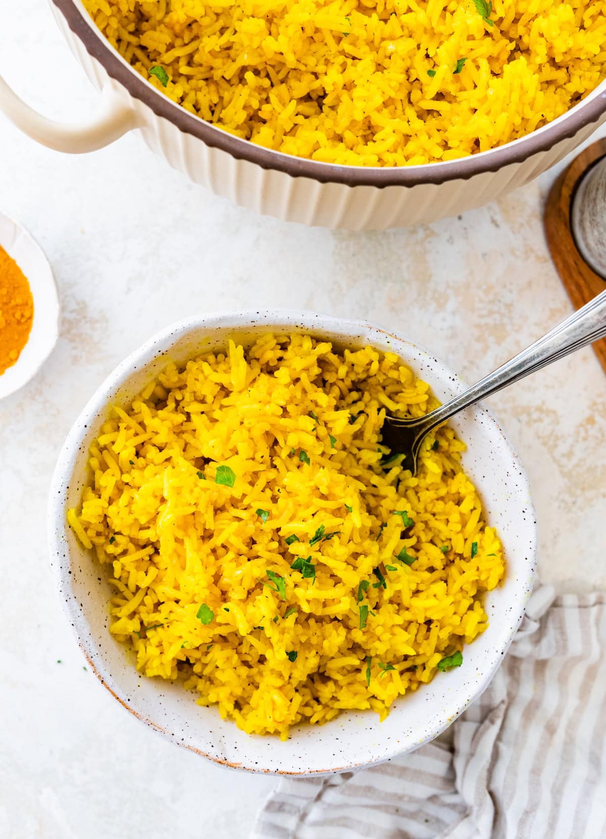 A bowl of turmeric rice served with a silver spoon. The rice is topped with fresh parsley.