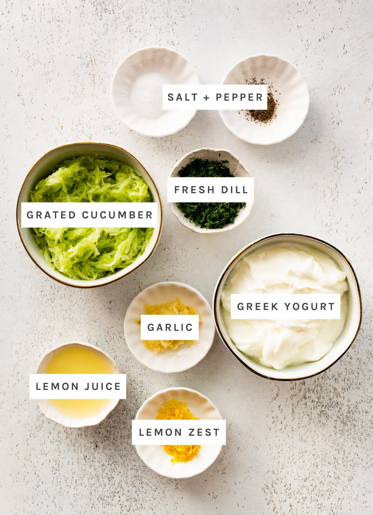 Ingredients measured out to make Easy Tzatziki: Salt+Pepper, Lemon Juice, Lemon Zest, Garlic, Greek Yogurt, Grated Cucumber, Fresh Dill.