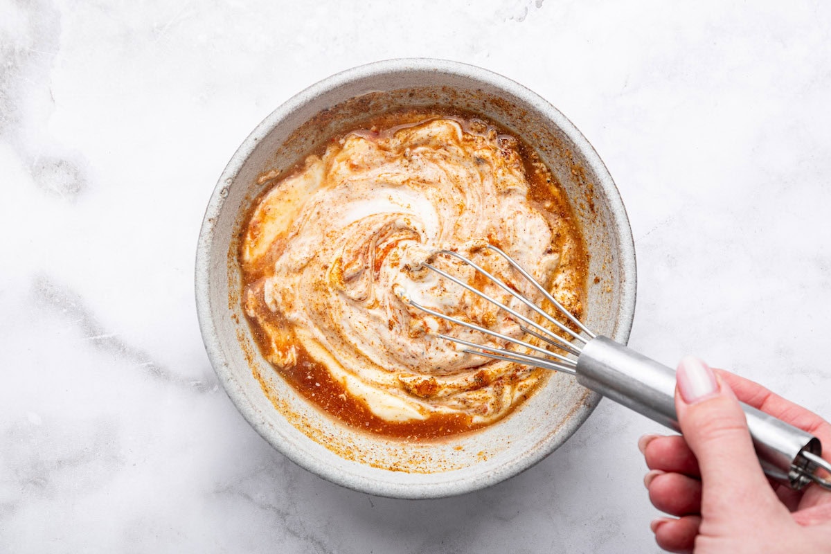 A woman's hand whisking together the yum yum sauce in a small ceramic bowl.