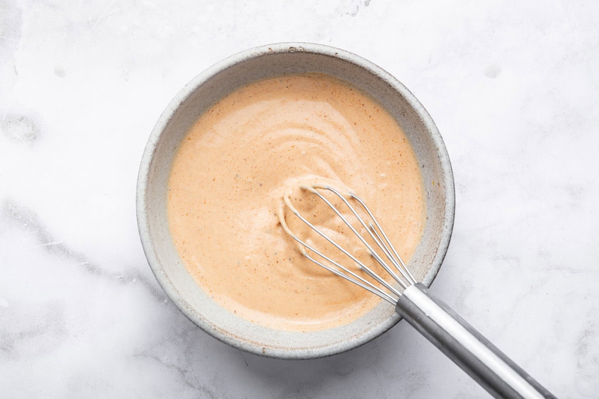 A silver whisk mixing together the homemade yum yum sauce recipe in a small ceramic bowl.