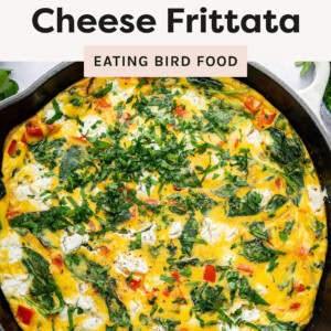 Photo is a freshly baked frittata in a cast-iron skillet, filled with vibrant spinach, red bell peppers, caramelized onions, and creamy goat cheese. The golden egg base is speckled with melted cheese and topped with freshly chopped herbs for a flavorful finish. The skillet sits on a rustic surface, surrounded by ingredients like goat cheese and cracked black pepper, adding to the inviting presentation.
