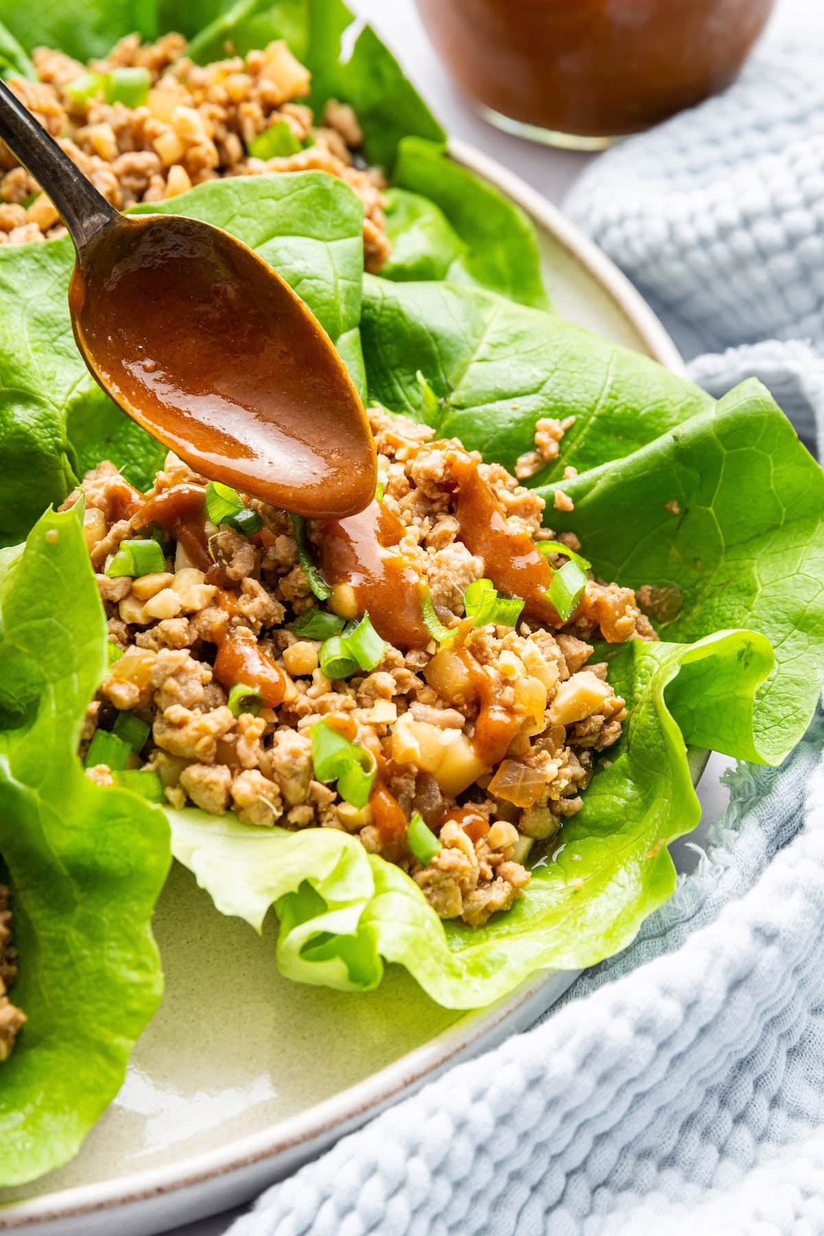 A spoon drizzling a peanut sauce over chicken lettuce wraps served on a plate.