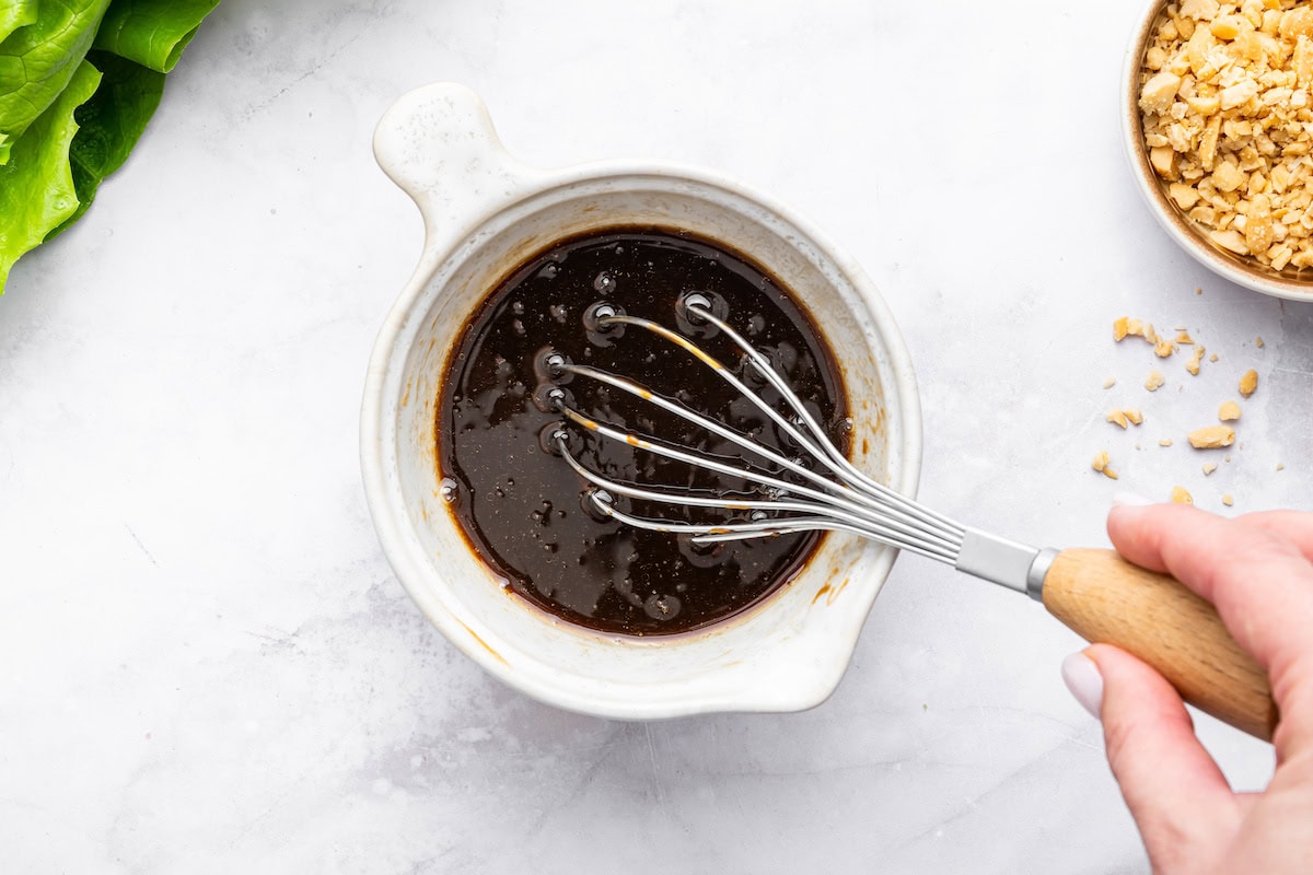 A woman's hand whisking the hoisin sauce for the ground chicken lettuce wraps.