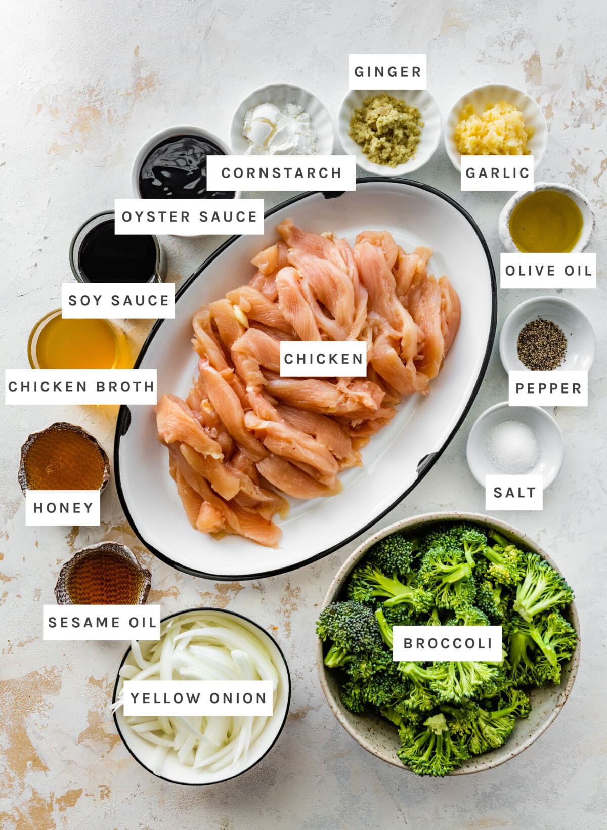 Ingredients measured out to makeChicken and Broccoli Stir Fry: Chicken, cornstarch, ginger, garlic, olive oil, pepper, salt, broccoli, yellow onion, sesame oil, honey, chicken broth, soy sauce, oyster sauce.