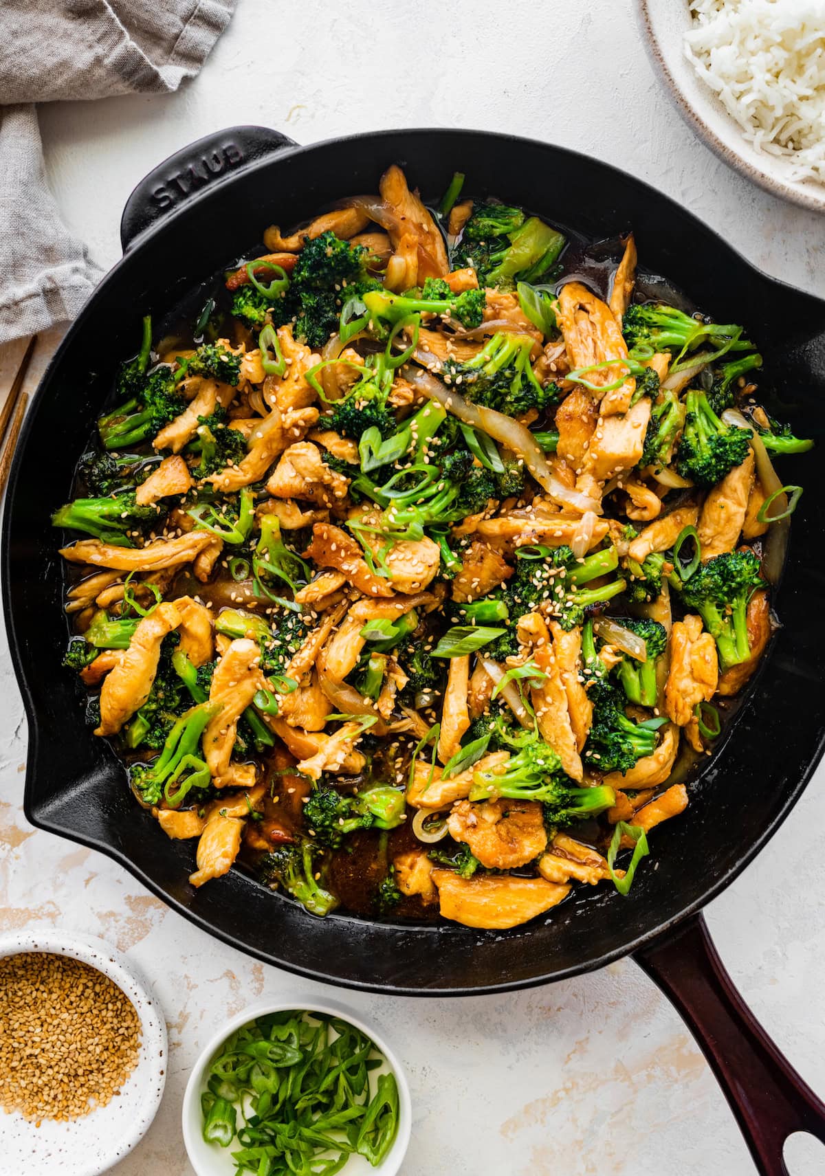 Chicken and broccoli stir fry in a cast iron skillet, garnished with sesame seeds and sliced green onions.