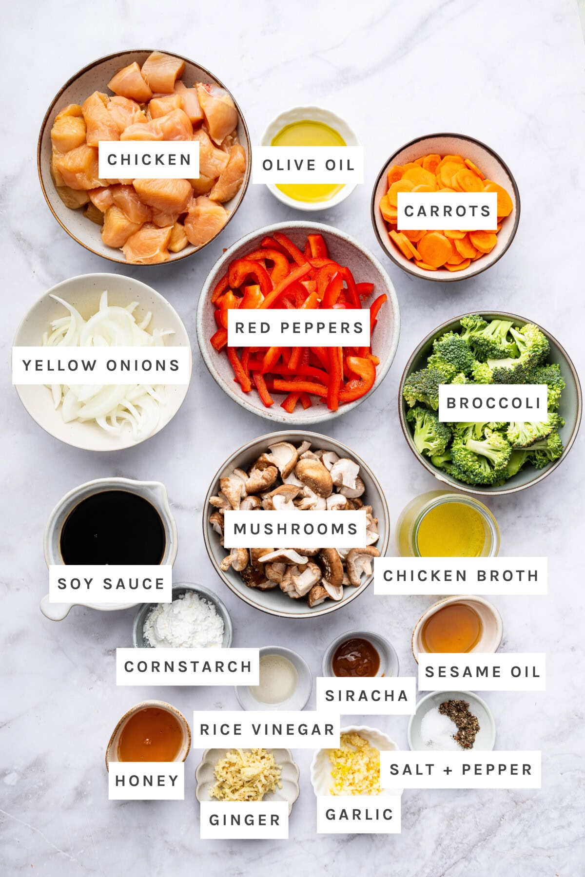Ingredients measured out to make Chicken Stir Fry: Chicken, olive oil, carrots, yellow onions, red peppers, broccoli, mushrooms, chicken broth, soy sauce, cornstarch, rice vinegar, siracha, sesame oil, honey, ginger, garlic, salt, pepper.