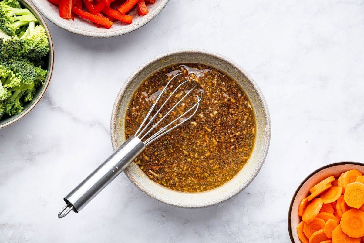 The chicken stir fry sauce whisked together in a small bowl. The silver whisk is in the bowl.