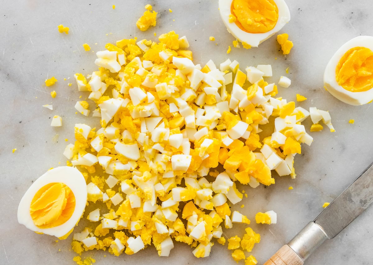 Chopped hard boiled eggs on a granite countertop next to a knife and three hard boiled egg halves.