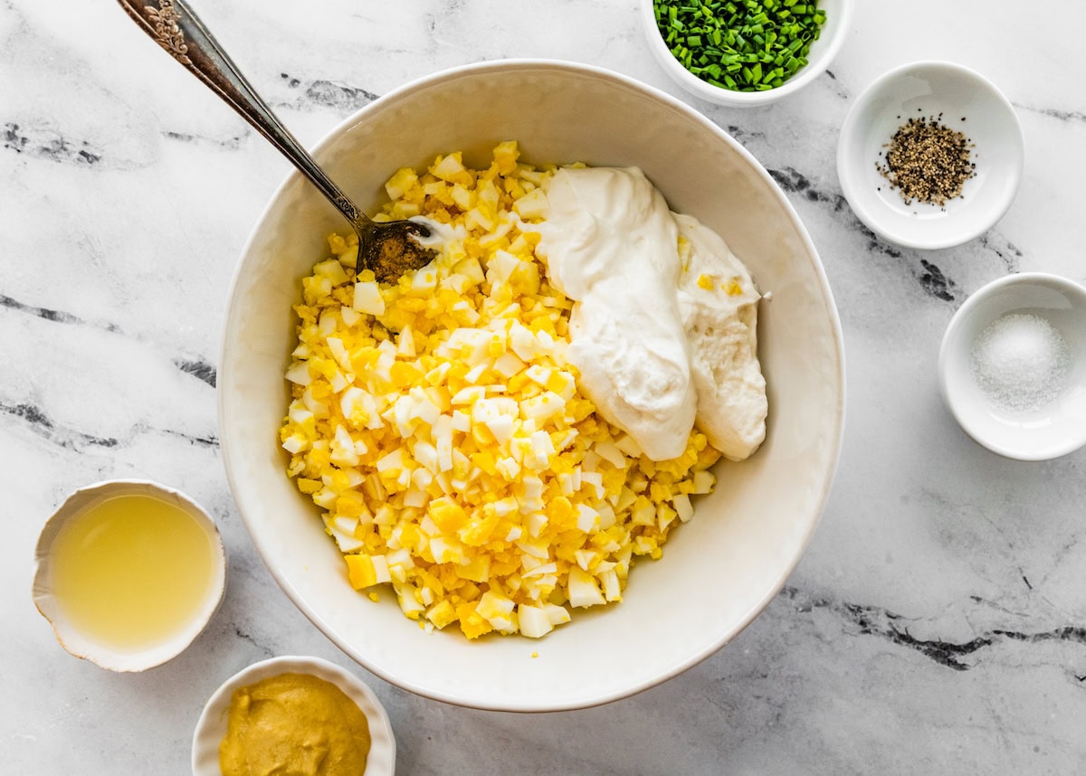 Chopped hard boiled eggs in a white ceramic bowl with blended cottage cheese. There's a silver spoon in the bowl.