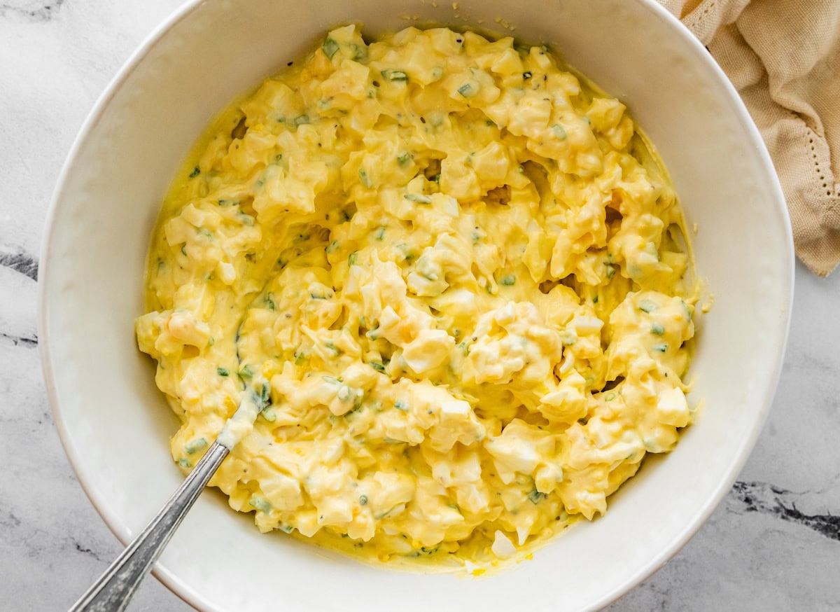 Mixed together cottage cheese egg salad in a ceramic white bowl served with a silver spoon.