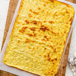 A baked cottage cheese flatbread on parchment paper on top of a wooden cutting board.