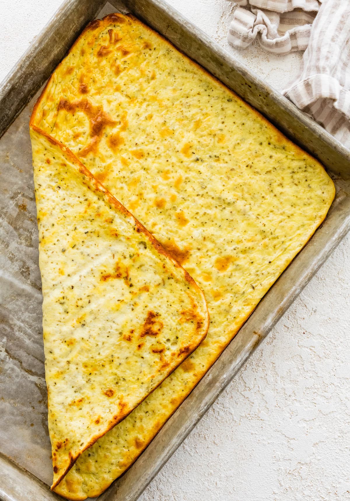 A baked cottage cheese flatbread on a small baking tray. One edge of the flatbread is flipped up so you can see the underside of the flatbread.