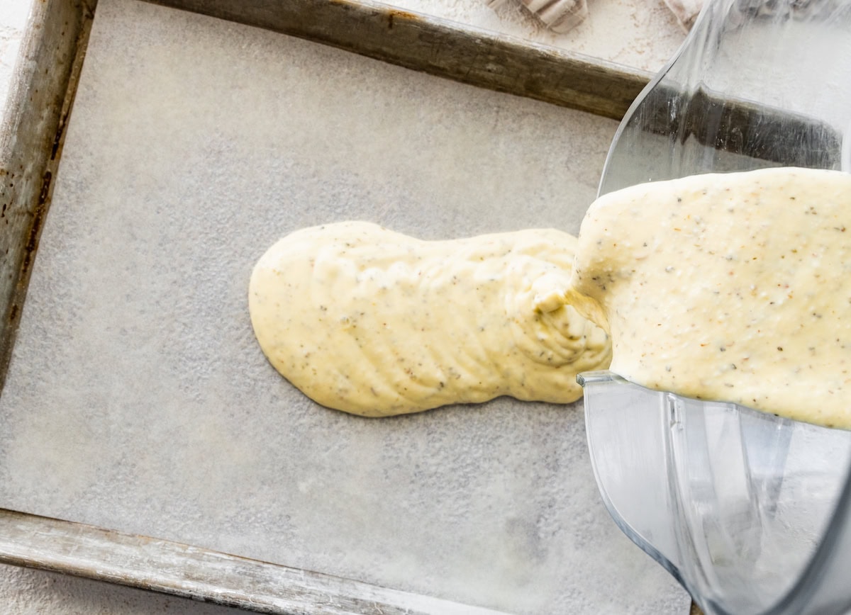 The cottage cheese flatbread mixture being poured onto a baking sheet lined with parchment paper.