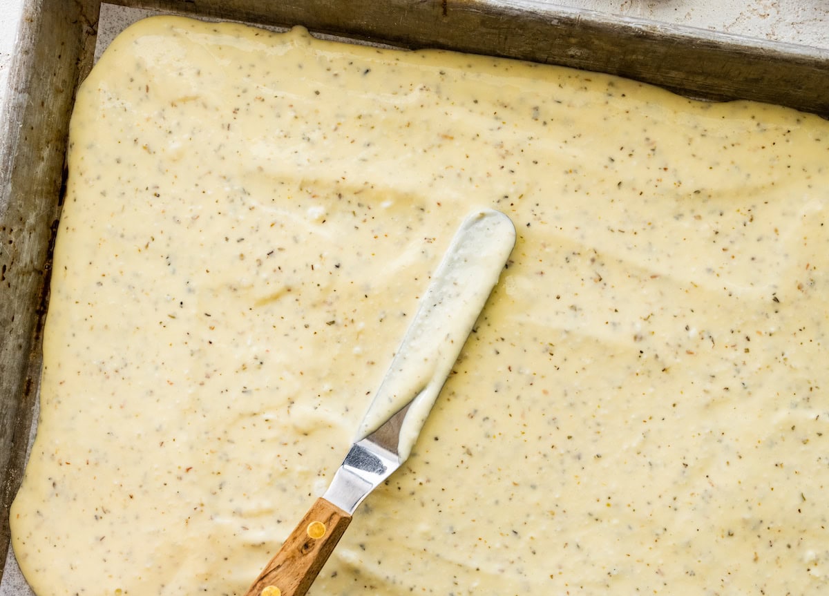 The cottage cheese flatbread mixture being spread out with a spatula on a small baking tray.