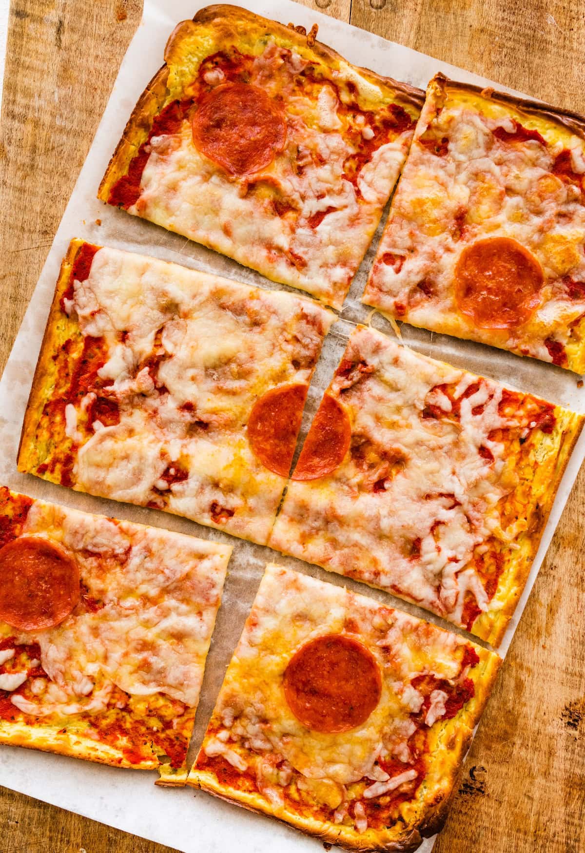 Six slices of a cottage cheese flatbread pizza topped with shredded cheese and pepperoni on a wooden cutting board.