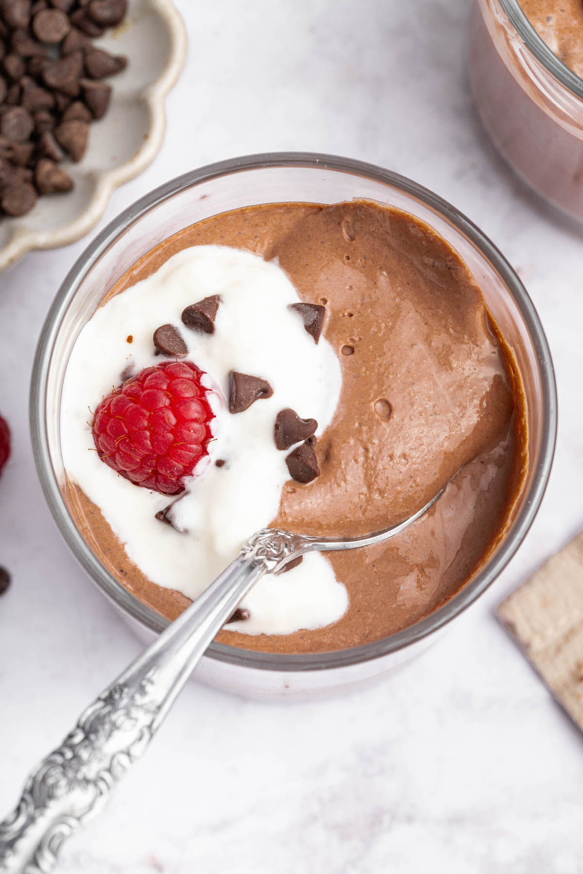 Cottage cheese chocolate topped with whip cream, chocolate chips and fresh raspberries. A silver spoon is in the mousse.