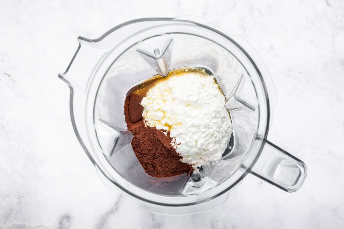 The ingredients for the cottage cheese mousse in the base of a blender: cottage cheese, cocoa powder and maple syrup.
