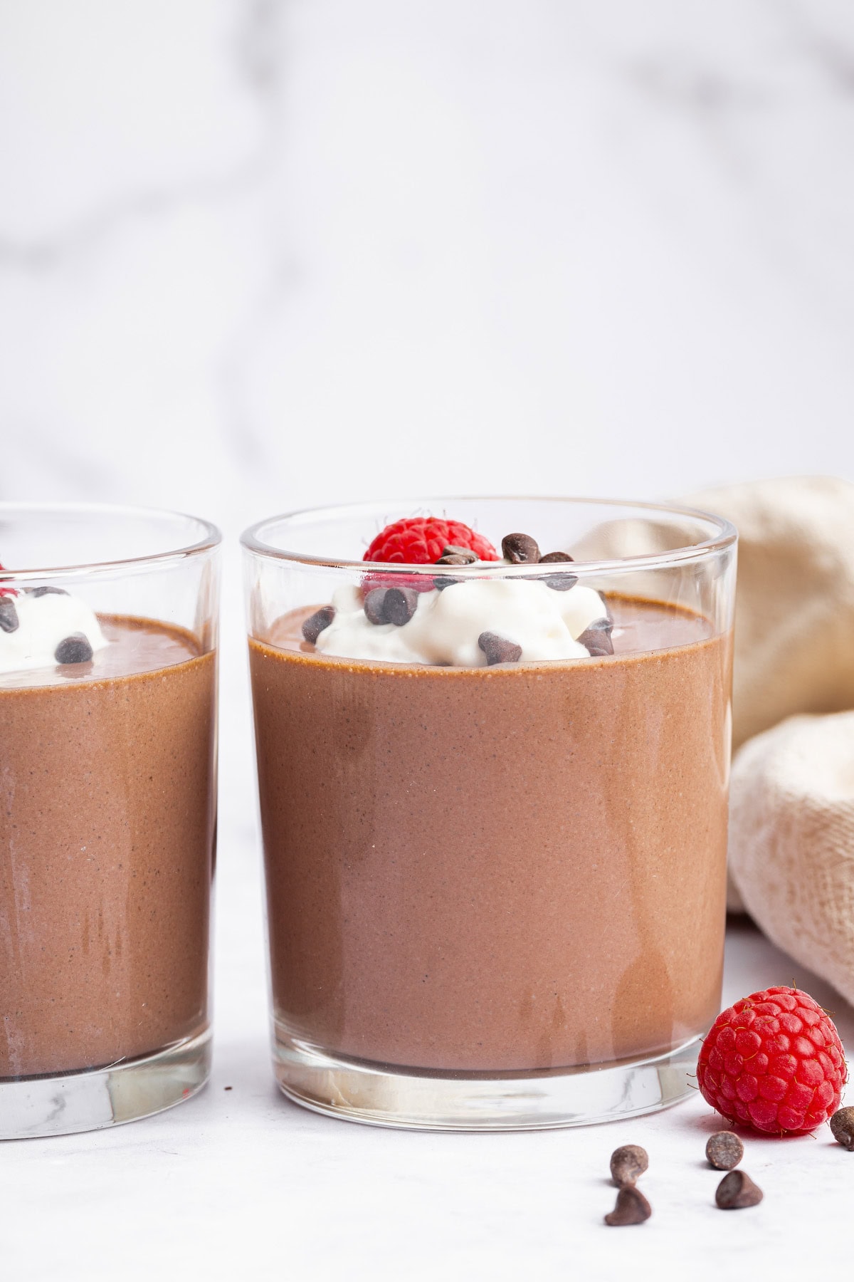 Cottage cheese chocolate mousse in two glasses topped with whip cream, chocolate chips and fresh raspberries.