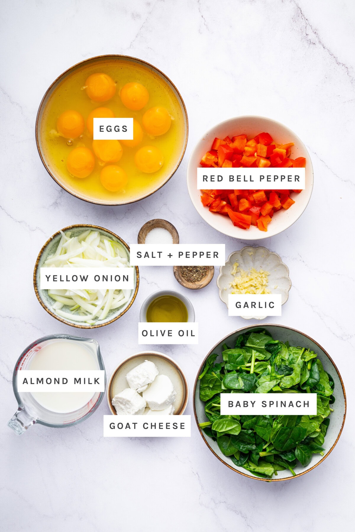 Ingredients measured out to make Easy Frittata with Caramelized Onions & Goat Cheese: Eggs, red bell pepper, yellow onion, salt + pepper, garlic, olive oil, almond milk, goat cheese, baby spinach.