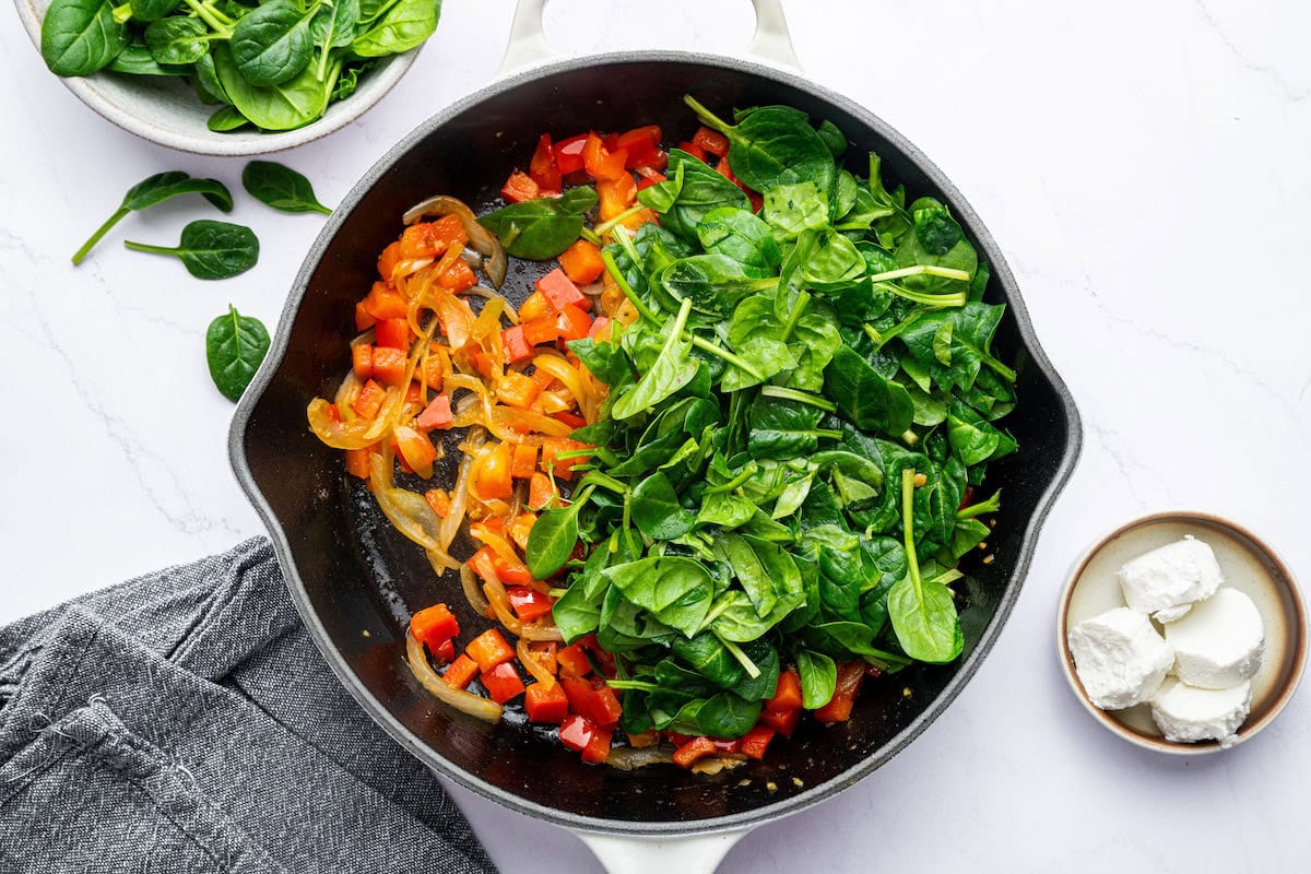 Fresh spinach added to the white cast iron skillet with the sautéed onions and bell peppers.