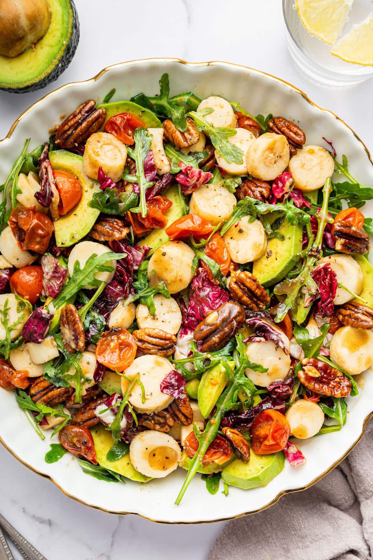 A large bowl of hearts of palm salad that has cherry tomatoes, arugula, avocado, pecans, and a honey balsamic dressing.