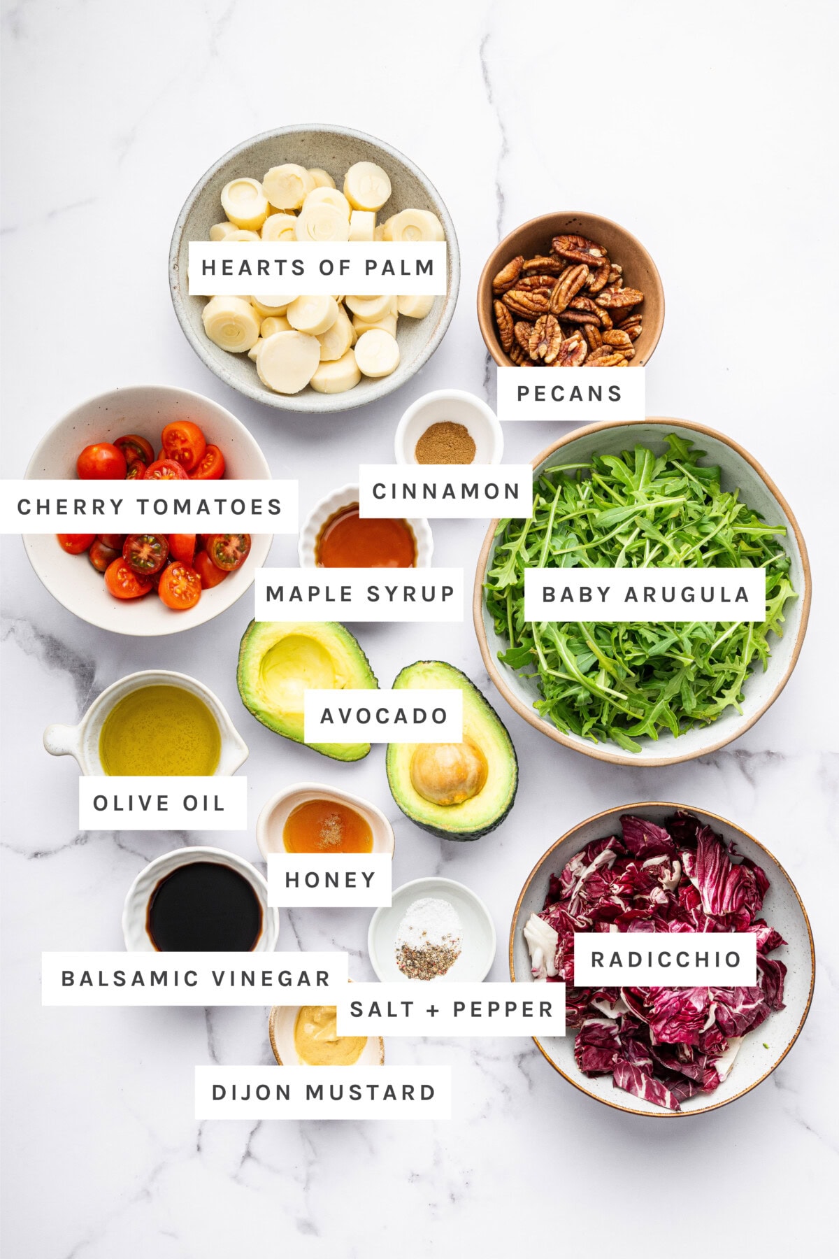 Ingredients for hearts of palm salad: hearts of palm, pecans, cinnamon, maple syrup, cherry tomatoes, arugula, avocado, olive oil, honey, vinegar, salt, pepper, radicchio, and dijon mustard.
