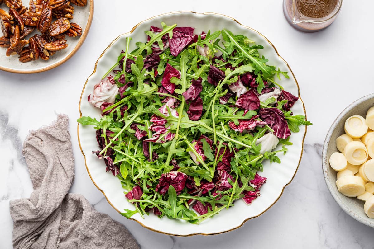 A large white serving bowl filled with a mix of fresh arugula and radicchio leaves.