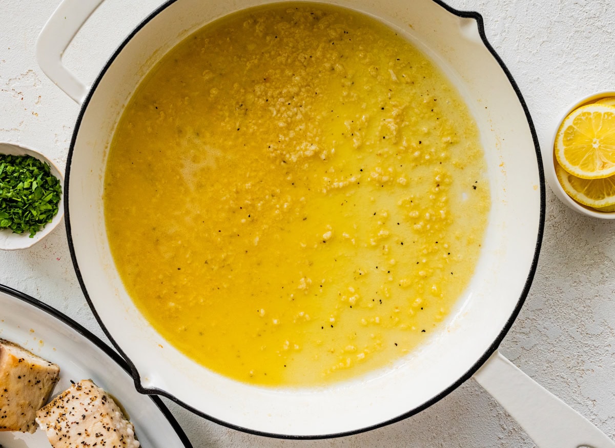 The lemon butter garlic sauce for the mahi mahi cooking in a white skillet.