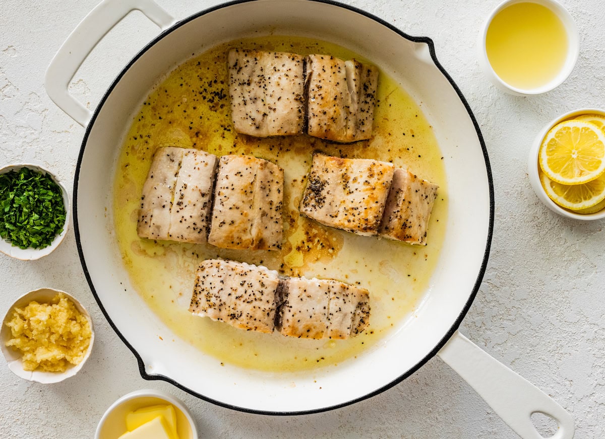 Four cooked mahi mahi fillets in the lemon butter garlic sauce in the white skillet.
