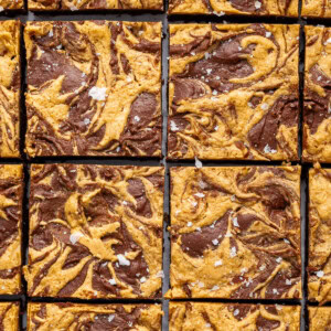 Peanut butter brownies cut into 16 squares. The brownies are topped with a peanut butter swirl and flaked sea salt.