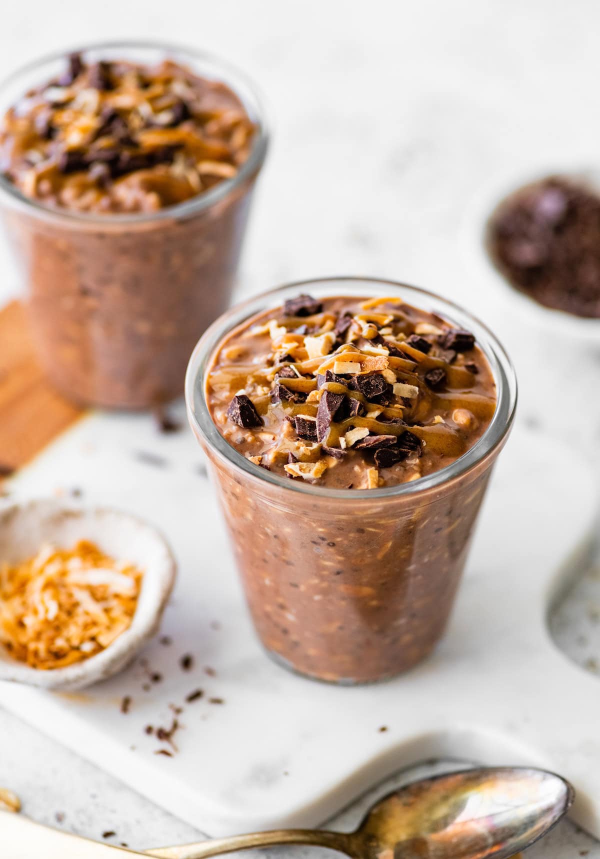 Two glass jars filled with samoas overnight oats. They're topped with chocolate chunks, date caramel and toasted coconut.