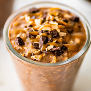 One glass jar filled with samoas overnight oats. It's topped with chocolate chunks, date caramel and coconut.