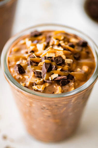 One glass jar filled with samoas overnight oats. It's topped with chocolate chunks, date caramel and coconut.