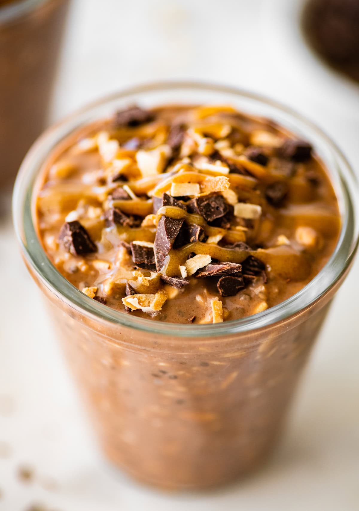 One glass jar filled with samoas overnight oats. It's topped with chocolate chunks, date caramel and toasted coconut.