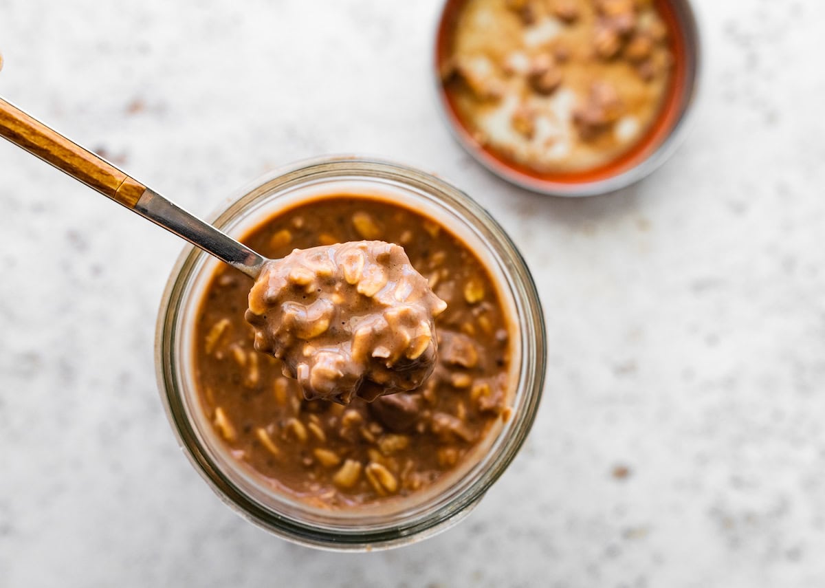 A spoon scooping out a bite of the samoas overnight oats from a glass jar.
